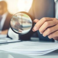 A man examines business documents with a magnifying glass