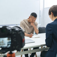 A camera filming a meeting between a black man and a female staff member