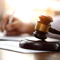 Judge writing legal documents while a gavel rests on paperwork, representing the principles of justice and law within the context of legal proceedings and courtroom activities