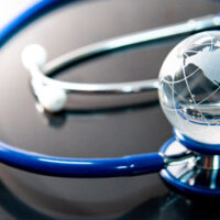 A stethoscope with a blue tube encircles a transparent globe with engraved continents, resting on a reflective surface, symbolizing global healthcare.